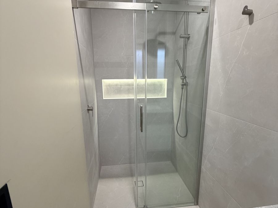 Walk-in shower with a sliding glass door and a lit recessed niche